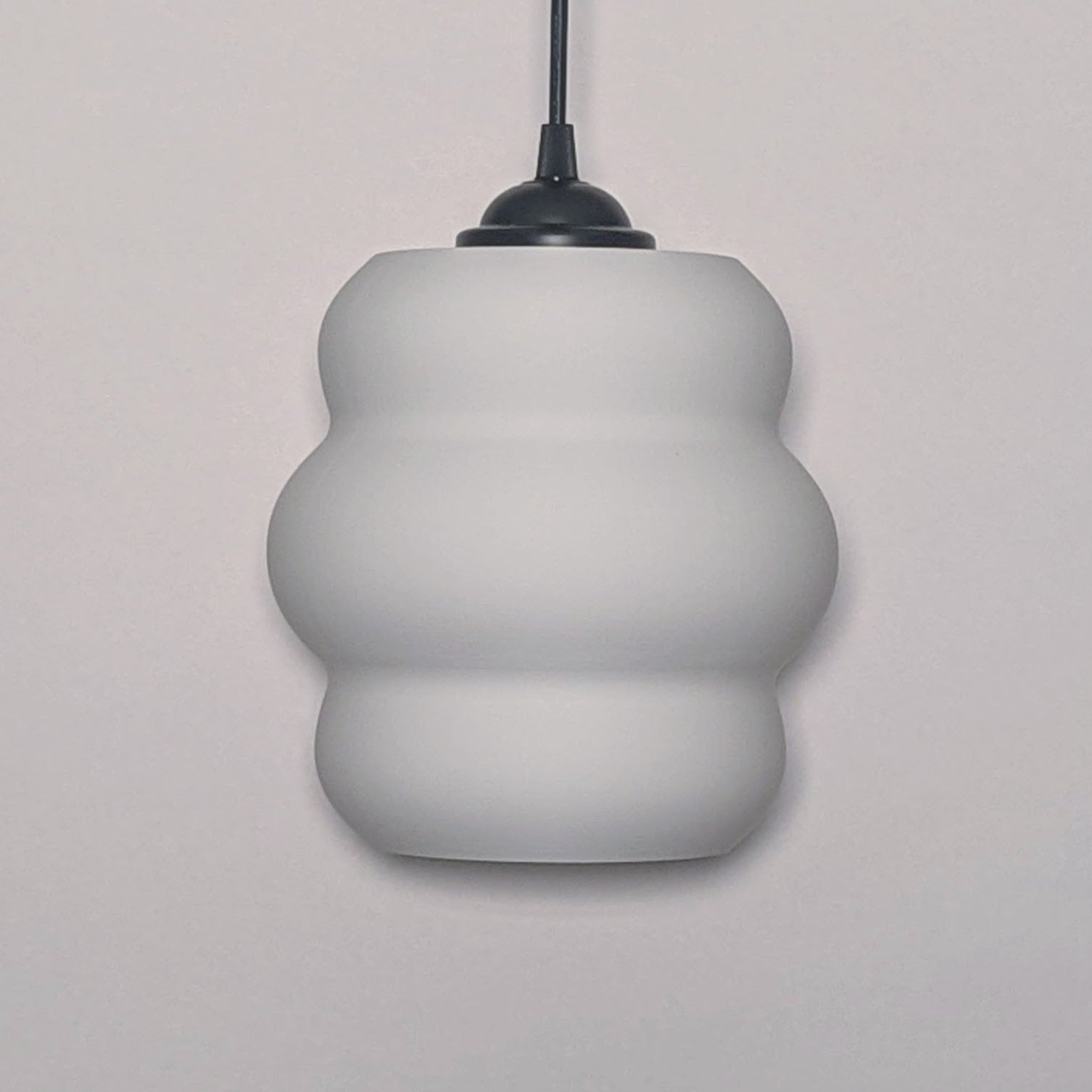 The Mammatus Pendant Light by Dryft Home features a modern, three-tiered bulbous design crafted from sustainable material. Its white form, suspended from a black cord, adds an eco-friendly touch that complements any decor.