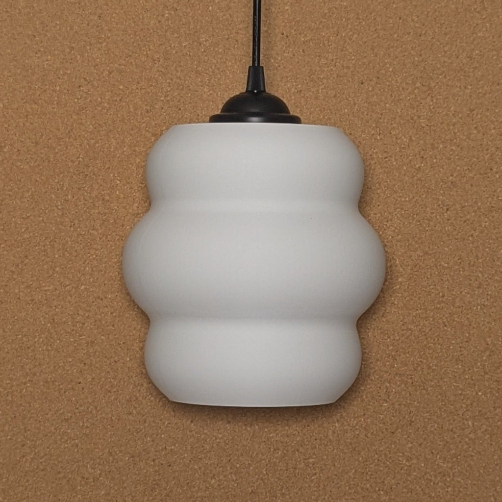 The Mammatus Pendant Light by Dryft Home, crafted from sustainable materials and featuring a wavy design, elegantly hangs from a black cord against a beige background.