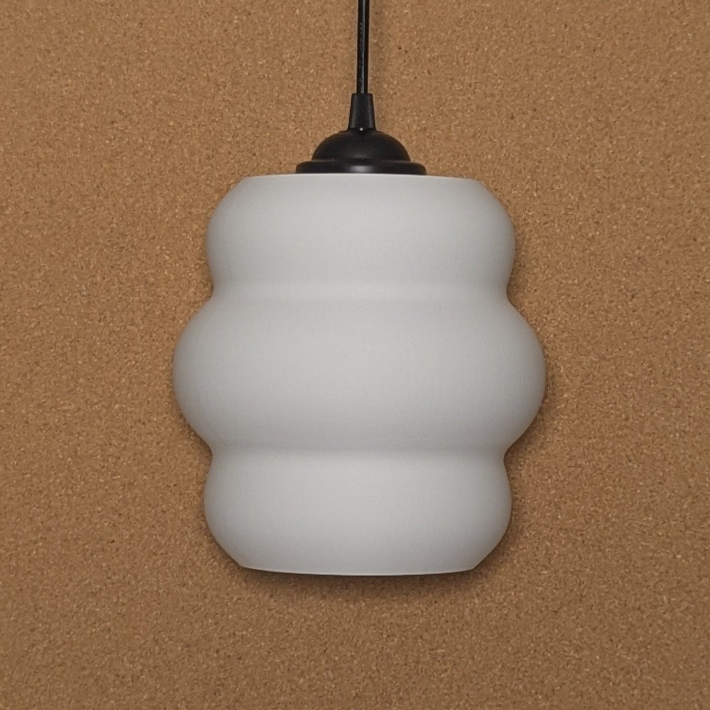 The Mammatus Pendant Light by Dryft Home, crafted from sustainable materials and featuring a wavy design, elegantly hangs from a black cord against a beige background.