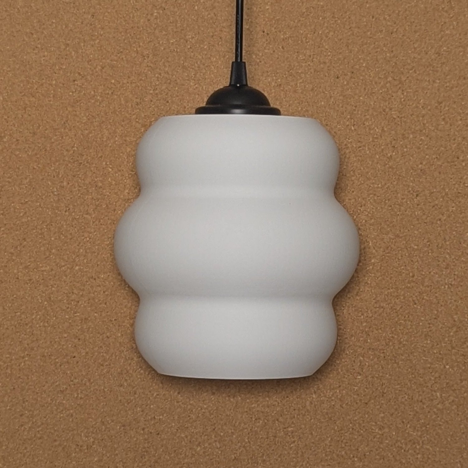 The Mammatus Pendant Light by Dryft Home, crafted from sustainable materials and featuring a wavy design, elegantly hangs from a black cord against a beige background.