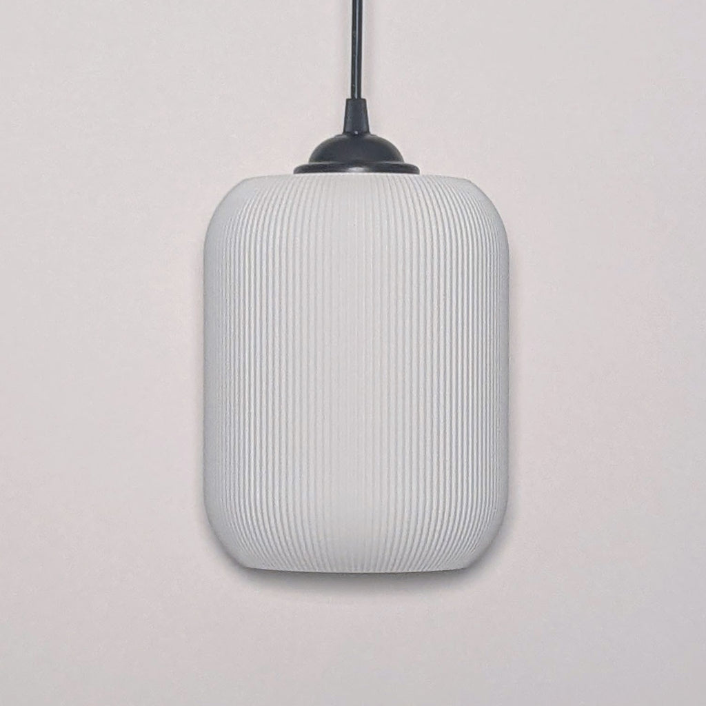 The Cumulis Pendant Light by Dryft Home showcases a modern design with a cylindrical textured white shade made from sustainable materials and a sleek black fixture, elegantly set against a plain white background.