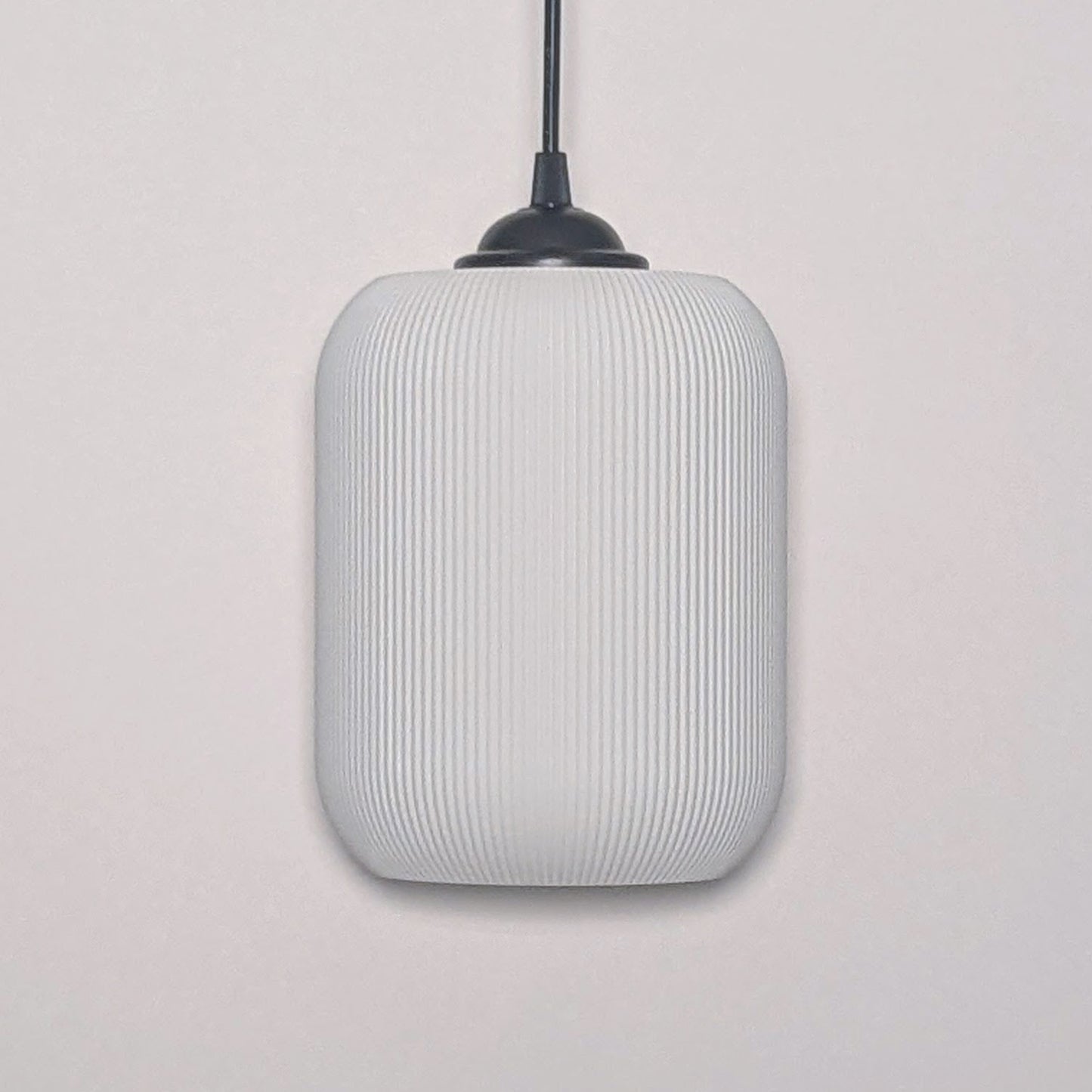 The Cumulis Pendant Light by Dryft Home showcases a modern design with a cylindrical textured white shade made from sustainable materials and a sleek black fixture, elegantly set against a plain white background.