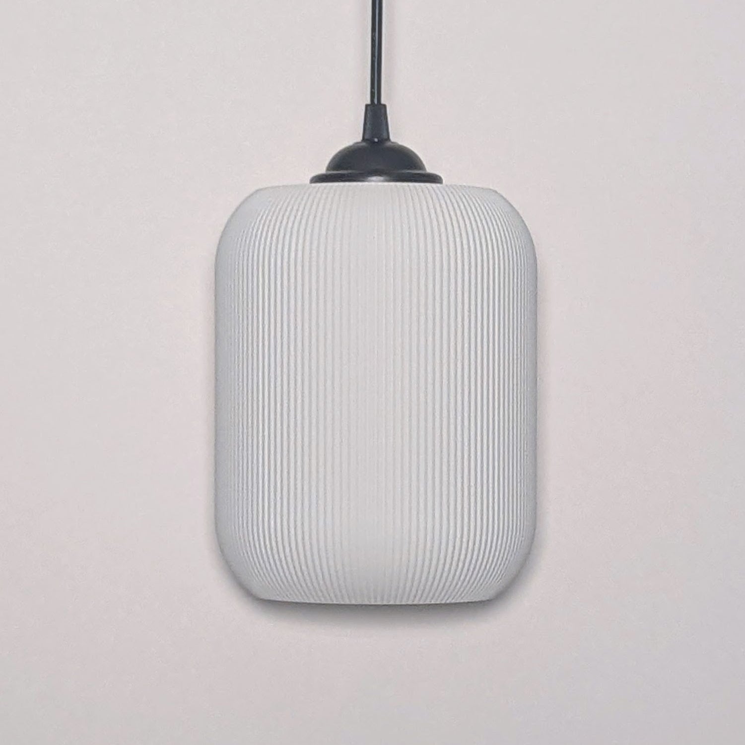 The Cumulis Pendant Light by Dryft Home showcases a modern design with a cylindrical textured white shade made from sustainable materials and a sleek black fixture, elegantly set against a plain white background.