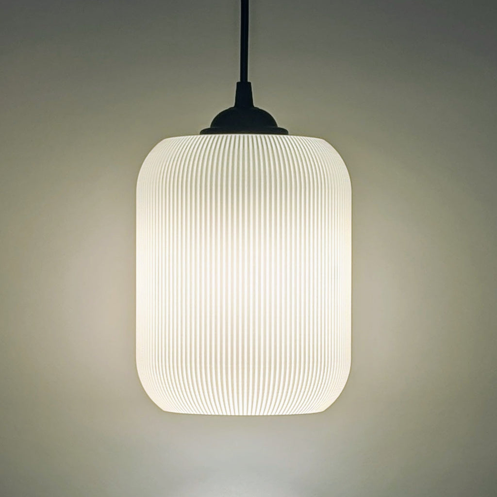 The Cumulis Pendant Light by Dryft Home features a modern cylindrical design with a ribbed translucent shade, crafted using 3D printing. Hanging from a black cord, it emits a soft warm glow against any neutral backdrop.