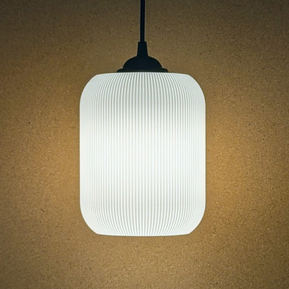 The Cumulis Pendant Light by Dryft Home boasts a ribbed, white cylindrical shade made with 3D printing and sustainable materials. It hangs on a sleek black cord against a beige backdrop, casting a warm glow perfect for modern spaces.