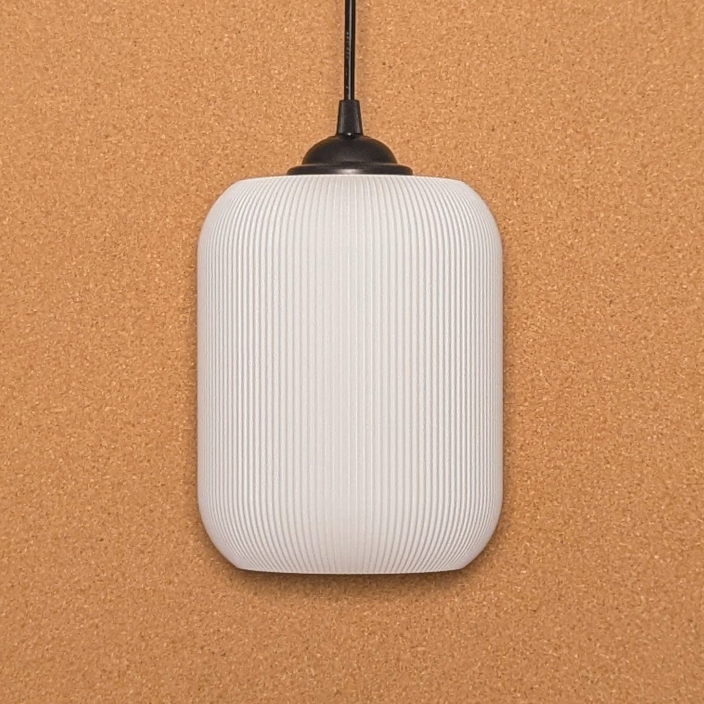 Crafted from sustainable materials using 3D printing, Dryft Homes Cumulis Pendant Light features a ribbed white cylindrical shade on a black cord, set against a textured cork background.