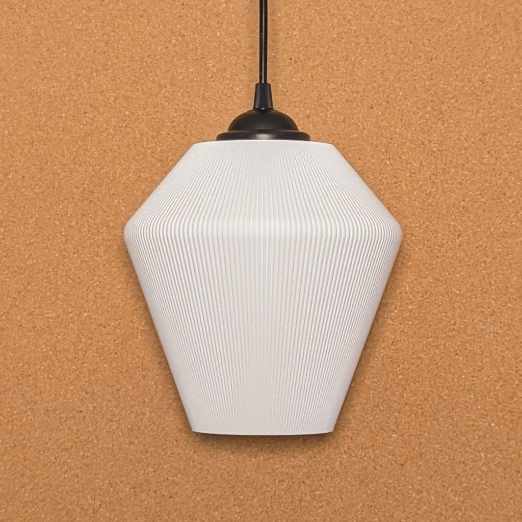 The Inversis Pendant Light by Dryft Home is made from sustainable materials, showcasing a white geometric form with a ribbed texture. It hangs elegantly from a black cord against a cork backdrop, featuring an angular polygonal design that brings modern elegance to any room.