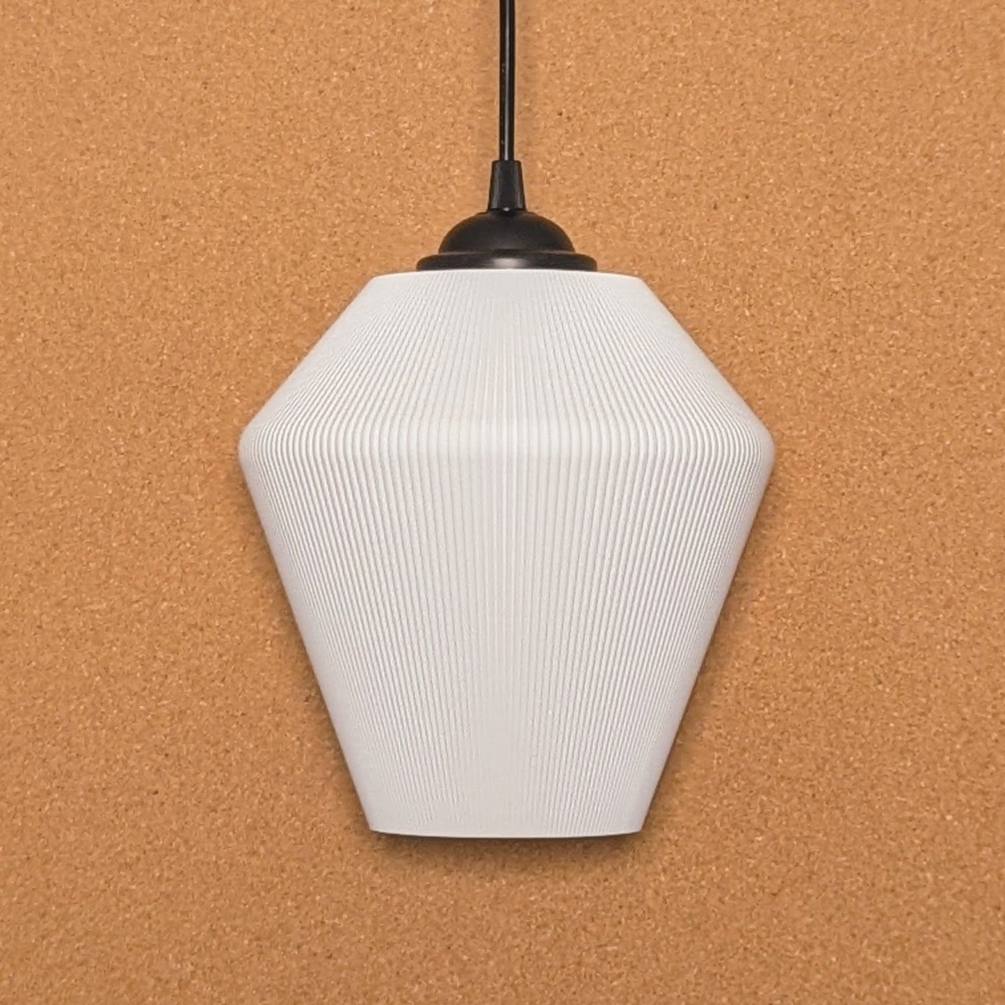 The Inversis Pendant Light by Dryft Home is made from sustainable materials, showcasing a white geometric form with a ribbed texture. It hangs elegantly from a black cord against a cork backdrop, featuring an angular polygonal design that brings modern elegance to any room.