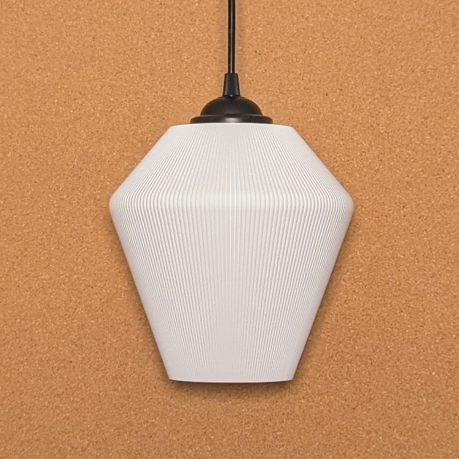 The Inversis Pendant Light by Dryft Home is made from sustainable materials, showcasing a white geometric form with a ribbed texture. It hangs elegantly from a black cord against a cork backdrop, featuring an angular polygonal design that brings modern elegance to any room.