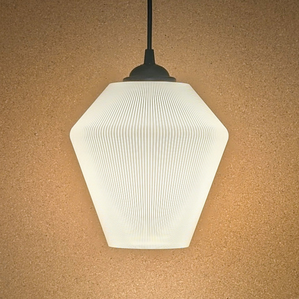 The Inversis Pendant Light by Dryft Home features a modern geometric design with a ribbed hexagonal shade, elegantly displayed against a beige textured wall. Made from sustainable materials, it emits a soft, warm glow.