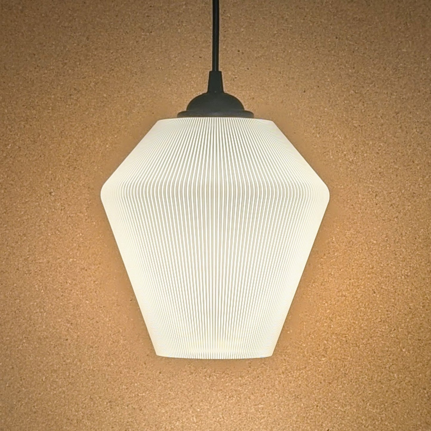 The Inversis Pendant Light by Dryft Home features a modern geometric design with a ribbed hexagonal shade, elegantly displayed against a beige textured wall. Made from sustainable materials, it emits a soft, warm glow.