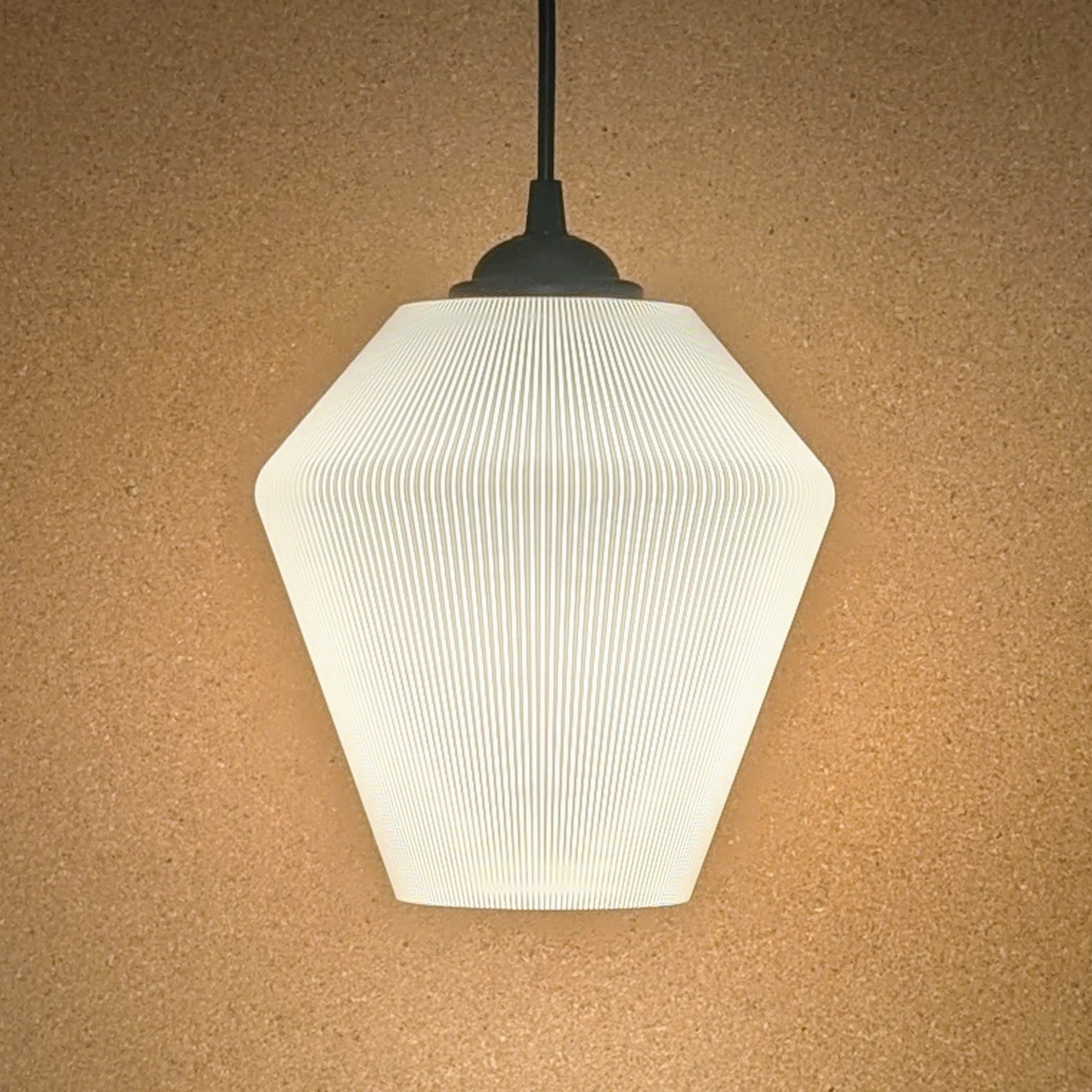 The Inversis Pendant Light by Dryft Home features a modern geometric design with a ribbed hexagonal shade, elegantly displayed against a beige textured wall. Made from sustainable materials, it emits a soft, warm glow.