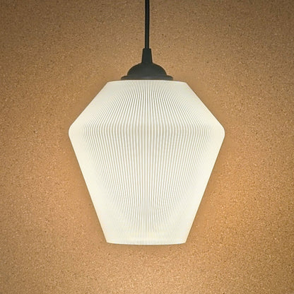 The Inversis Pendant Light by Dryft Home features a modern geometric design with a ribbed hexagonal shade, elegantly displayed against a beige textured wall. Made from sustainable materials, it emits a soft, warm glow.