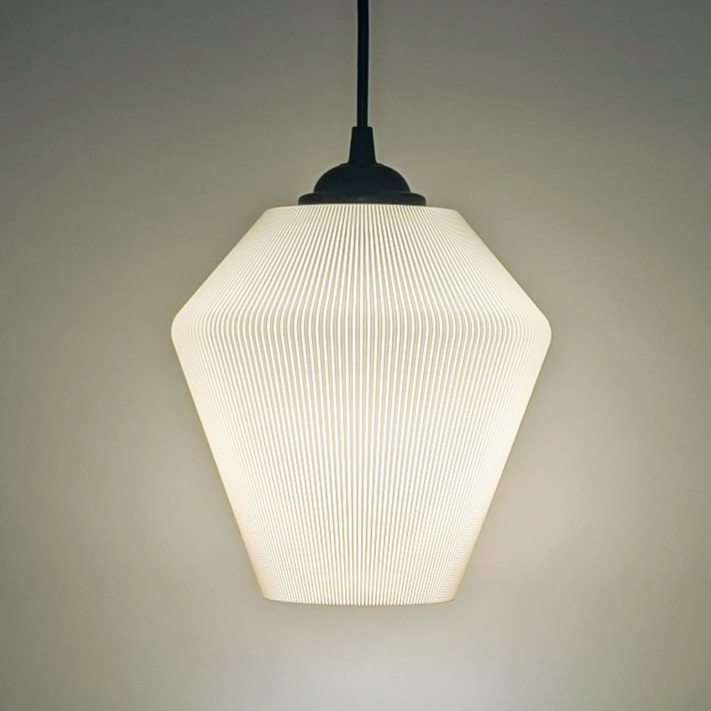 The Inversis Pendant Light by Dryft Home is a modern, minimalist fixture made from sustainable materials. It features a textured geometric shade that casts a soft, warm glow against plain backgrounds, creating a cozy ambiance.