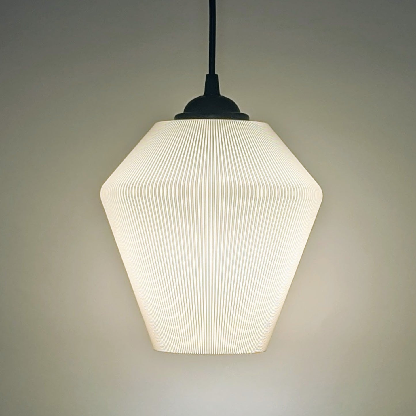 The Inversis Pendant Light by Dryft Home is a modern, minimalist fixture made from sustainable materials. It features a textured geometric shade that casts a soft, warm glow against plain backgrounds, creating a cozy ambiance.