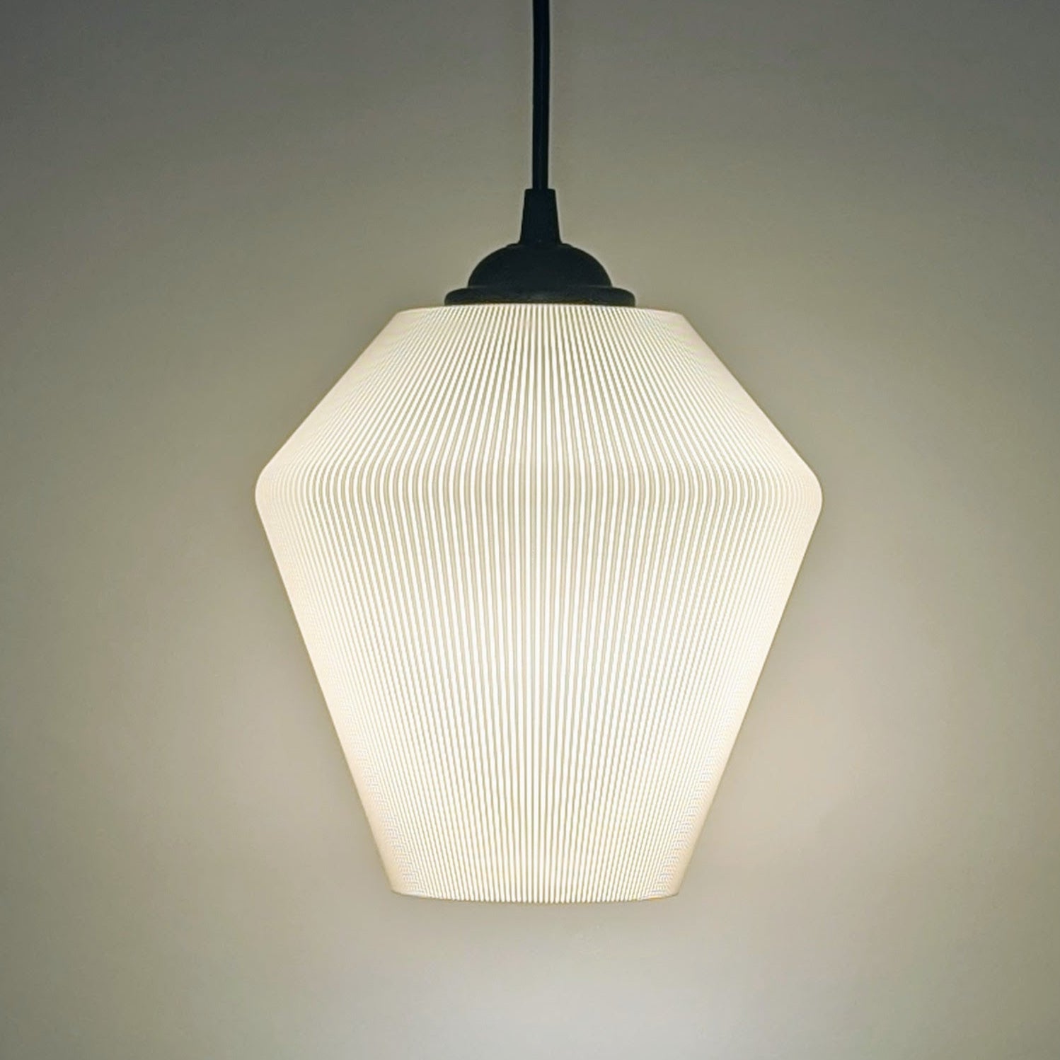 The Inversis Pendant Light by Dryft Home is a modern, minimalist fixture made from sustainable materials. It features a textured geometric shade that casts a soft, warm glow against plain backgrounds, creating a cozy ambiance.