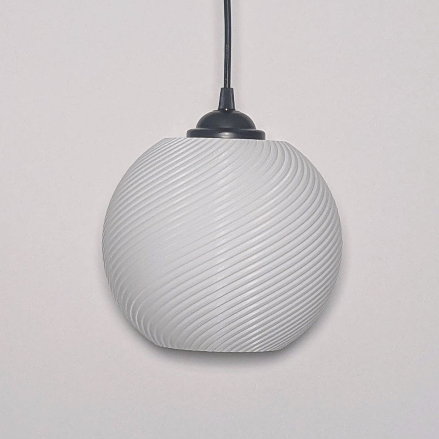 The Vortice Pendant Light by Dryft Home features a textured spiraling design, 3D printed from biodegradable PLA plastic. It hangs from a black cord against a plain white backdrop.