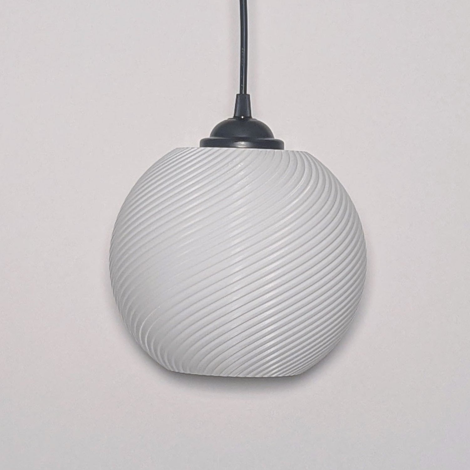 The Vortice Pendant Light by Dryft Home features a textured spiraling design, 3D printed from biodegradable PLA plastic. It hangs from a black cord against a plain white backdrop.