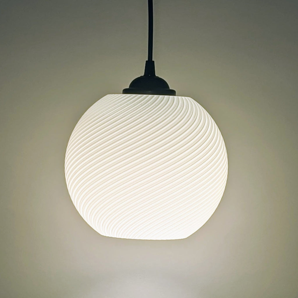 The Vortice Pendant Light by Dryft Home features a 3D printed, swirling pattern. Crafted from biodegradable PLA plastic, it emits a soft glow and hangs from a dark cord, exemplifying modern, sustainable lighting against a neutral background.