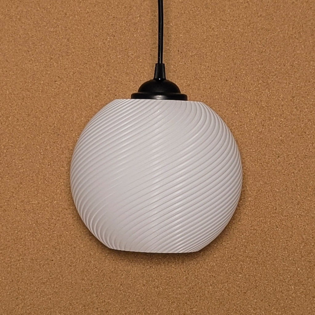 The Vortice Pendant Light by Dryft Home, made of biodegradable PLA plastic, features a spherical, white design with a spiral pattern. It hangs elegantly against a textured brown background with a black top attachment and an extending cord.