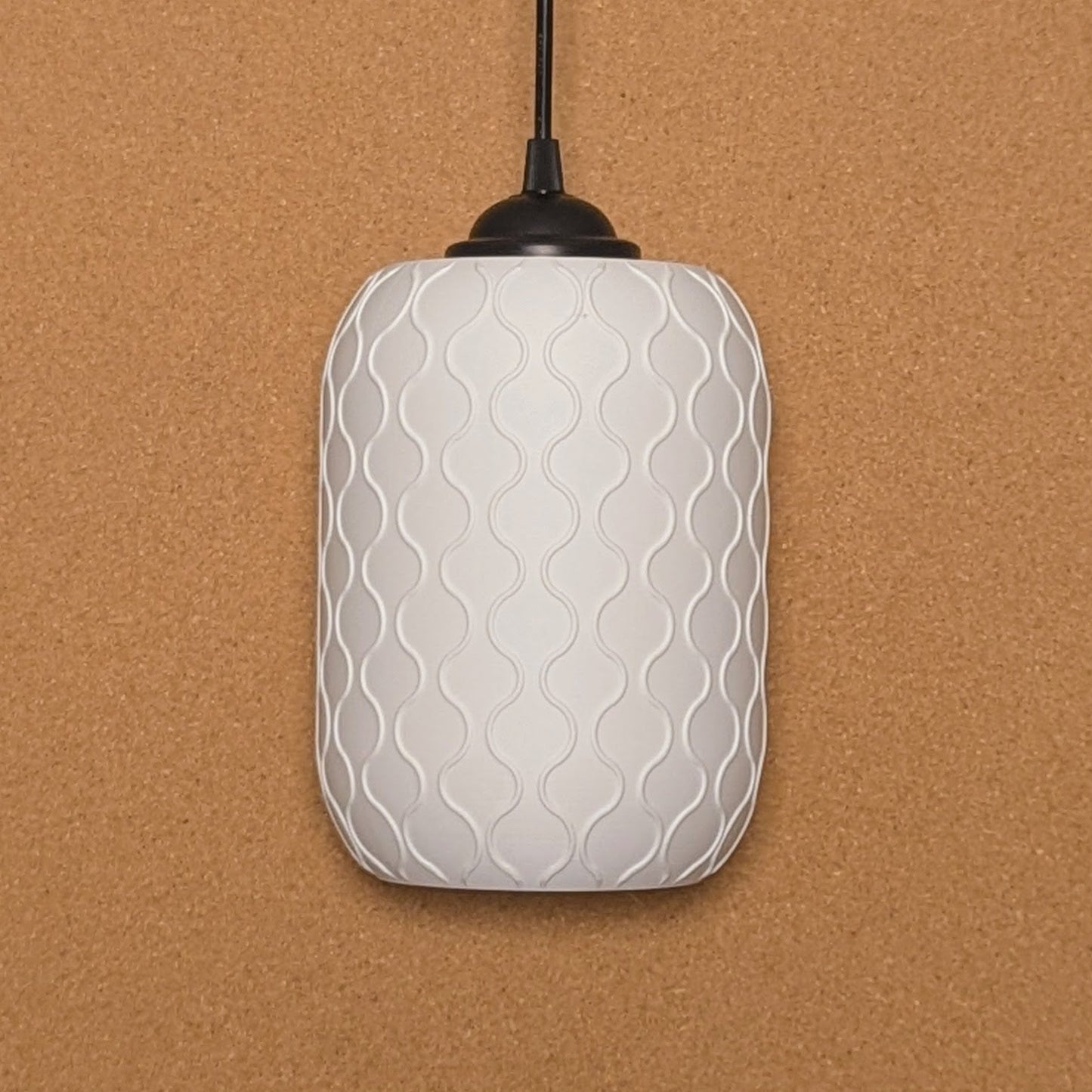 The Cirrus Pendant Light by Dryft Home features a white, textured, cylindrical design with a wavy pattern against a corkboard backdrop. Made from sustainable materials, it hangs elegantly with a black cord, showcasing eco-friendly elegance.