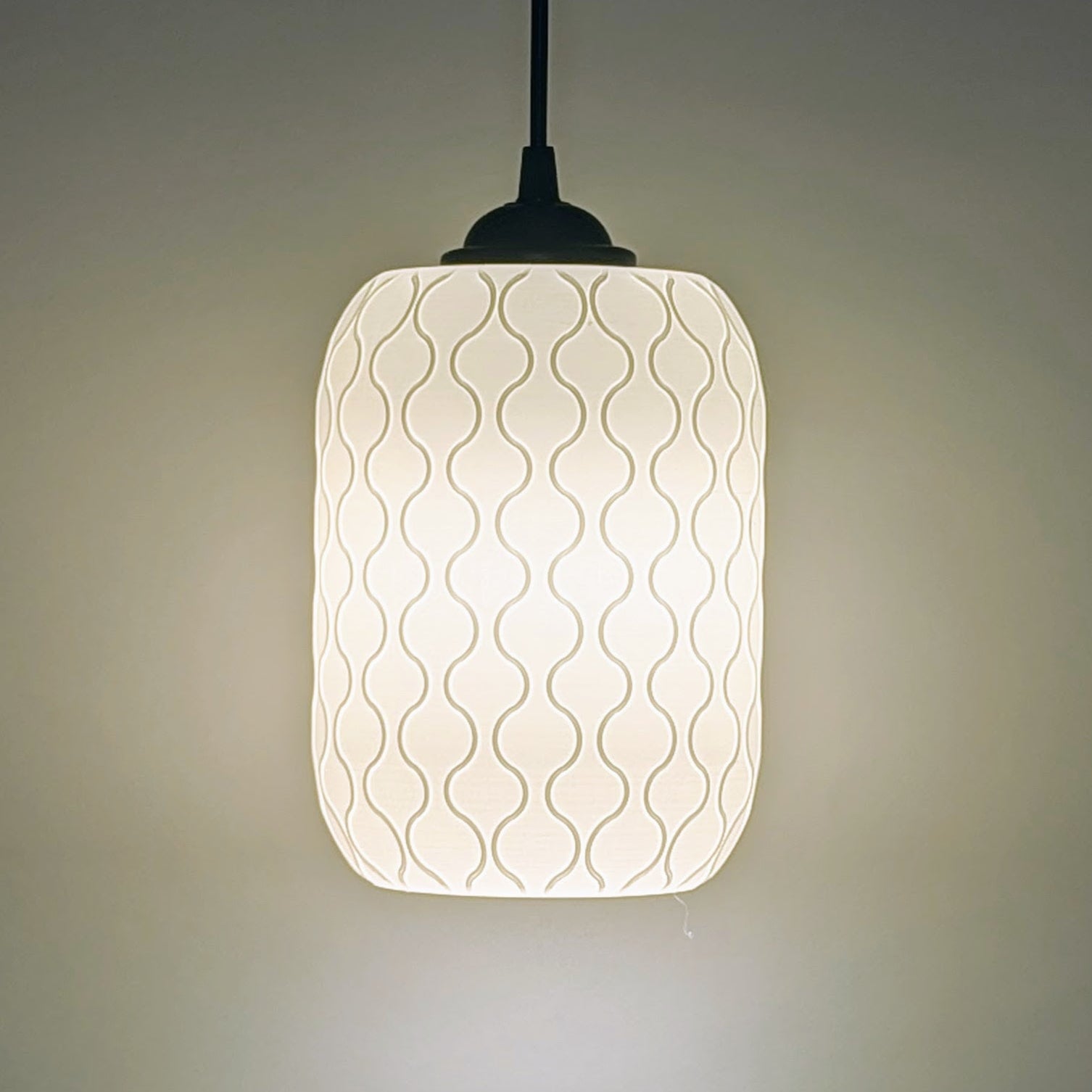The Cirrus Pendant Light by Dryft Home features a white cylindrical shade made from sustainable materials with a subtle wavy line pattern, casting a warm glow against a plain background.