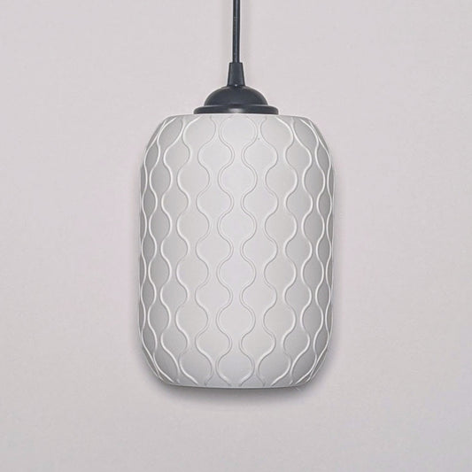 The Cirrus Pendant Light by Dryft Home is crafted from sustainable materials, featuring a smooth, cylindrical white shade. It hangs from a black cord and displays an intricately textured pattern of interlocking wavy lines, creating a subtle geometric design against the wall.