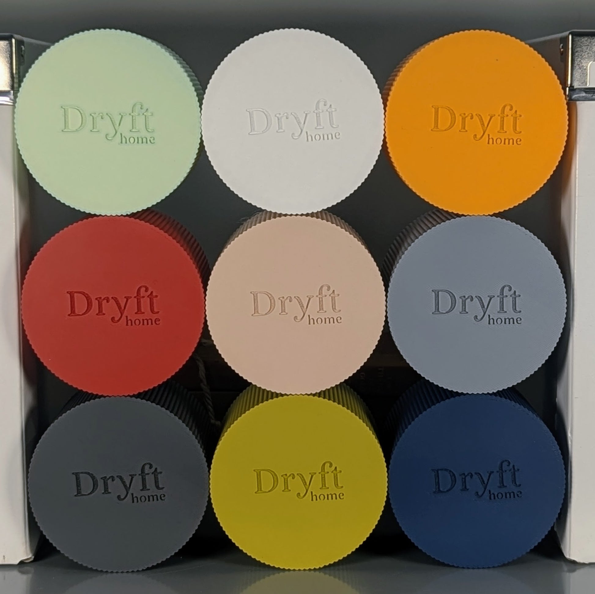 A display of nine circular pieces, adorned with Dryft Home branding, ranges in color from light green to dark blue and is crafted from biodegradable PLA plastic. This eco-friendly decor includes colors such as orange, red, beige, and more.