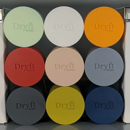 A display of nine circular pieces, adorned with Dryft Home branding, ranges in color from light green to dark blue and is crafted from biodegradable PLA plastic. This eco-friendly decor includes colors such as orange, red, beige, and more.
